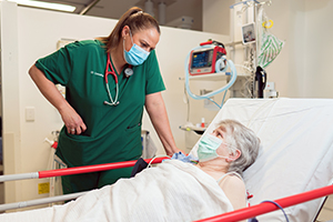 A female doctor talks with an older female patient who is laying in a hospital bed