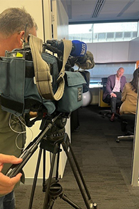 A camera operator films Professor Dickon Hayne speaking with a journalist.