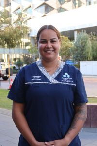 A portrait photo of Aboriginal Health Practitioner Liana Prosser standing in her uniform, outside of Fiona Stanley Hospital.