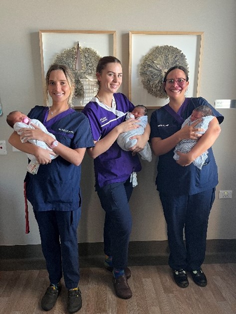 Three nurses in blue uniforms holding babies