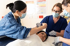 Three nurses stand beside a young woman who is laying on a bed.