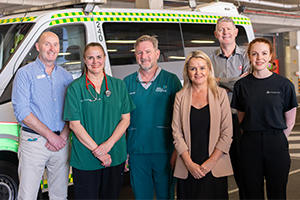 A group of six male and female health professionals stand beside an ambulance.