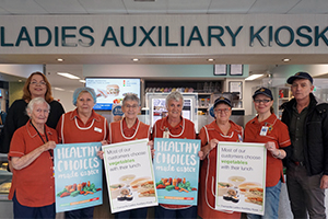 Fremantle Hospital kiosk volunteers and SMHS Health Promotion staff stand in front of the kiosk holding healthy food choices signage