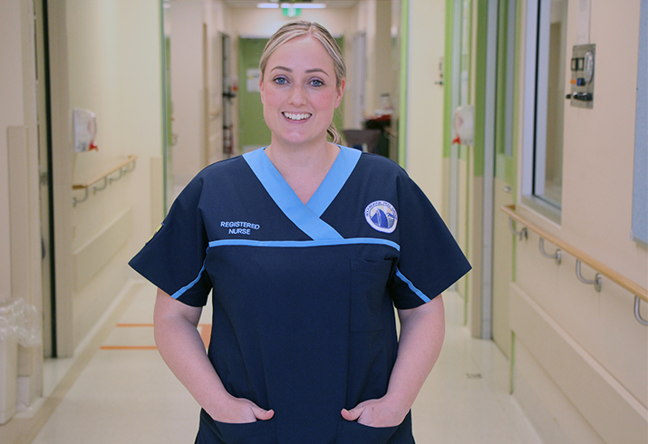 A female nurse wearing scrubs stands in a hospital hallway