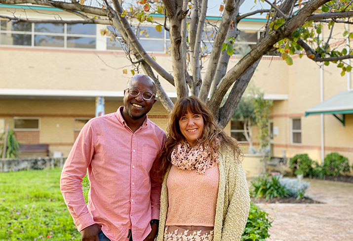 A man and a woman stand side by side smiling while outdoors