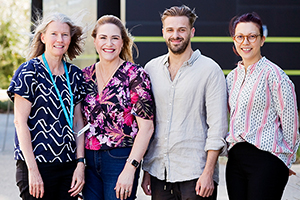 A group of three female and 1 male researcher stand together outside.