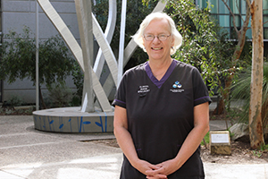 Cynthia Hawkes stands in front of a sculpture in a garden.