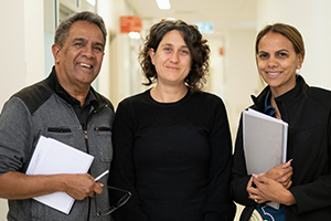 A male and female Aboriginal Health Liaison Officer stand either side of a female social worker in a corridor