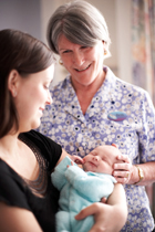 Woman holding a sleeping newborn baby while a midwife looks on.